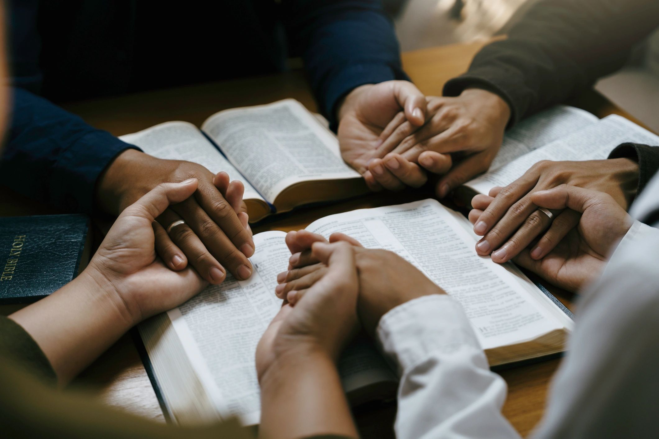 Hands joined in prayer around an open Bible